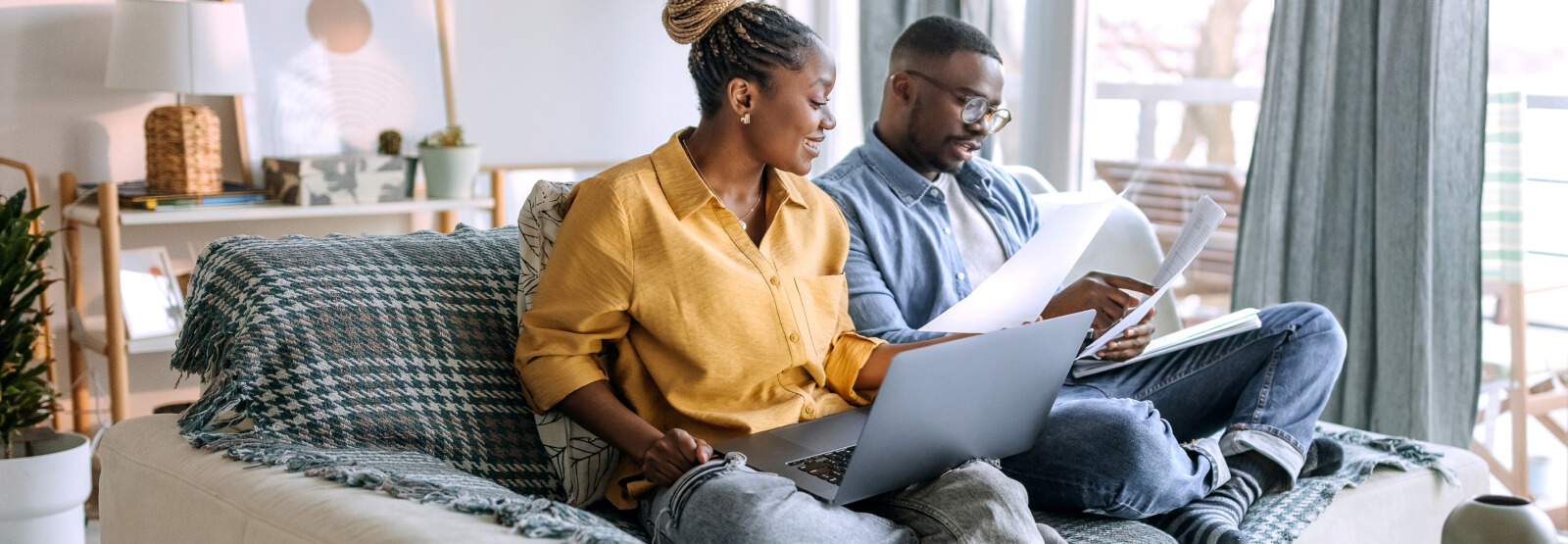 Couple reviewing paperwork while sitting on a couch with computer.